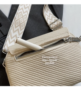 Detail of the back zipper pocket on a beige woven crossbody bag with chevron strap