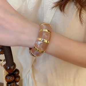 Macro detail of amber marbled resin and wavy gold metal segments on wide cuff bracelet