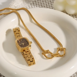 Detail of gold snake chain necklace and vintage square watch on a white ceramic plate