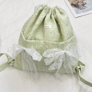 Detail of light green drawstring backpack with a large white lace bow and textured fabric