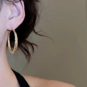 Close-up of golden round hoop earrings with unique twisted texture on model's ear