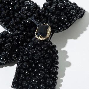 Detail view of black bow hair clip with heavy beading and central rectangular gemstone