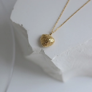 Macro shot of gold heart pendant with vintage floral relief on fine cross chain
