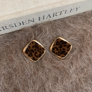 Detailed view of geometric acrylic leopard print earrings on soft brown fur and book