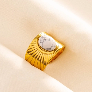 Detail of a gold sunburst ring featuring an oval white turquoise stone on satin fabric
