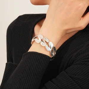 Detail of silver S-shaped irregular chain link bracelet on model's wrist with black knitwear