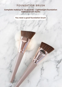 Flat lay of angled foundation brushes with wooden handles on white marble surface