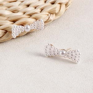 Macro shot of handmade bow earrings with woven faux pearls and delicate gold wire details