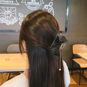 Detail of mesh bow hair claw with pearl tassel pendant worn by a model in a cafe