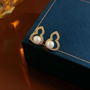 Golden gourd-shaped pearl stud earrings with crystal inlay on a dark blue jewelry box