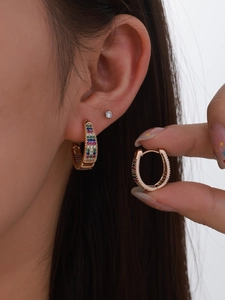 Detail of gold U-shaped huggie earrings with rainbow zircon stones on model's ear