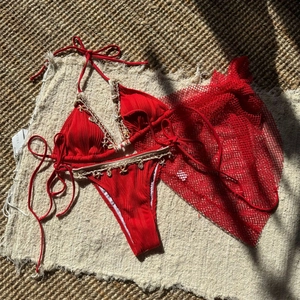 Detail of red bikini with white crochet trim and starfish charms on a woven mat