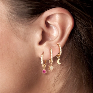 Close-up of three gold earrings with pink gemstone, star and moon pendants on ear