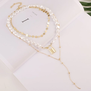 Detail of layered gold necklace with baroque pearls and a stylish lock pendant charm