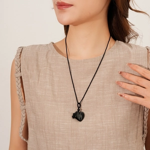 Detailed view of a black heart pendant on a woven cord necklace worn by a model