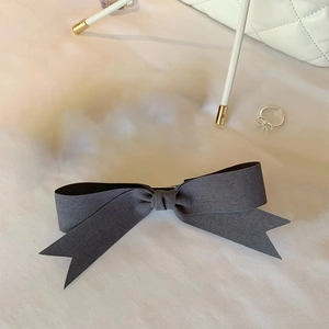Detail view of a gray satin bow hair clip with dovetail ends on soft white fabric