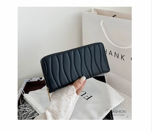 Close-up of black wavy quilted clutch purse with gold zipper held against gift box
