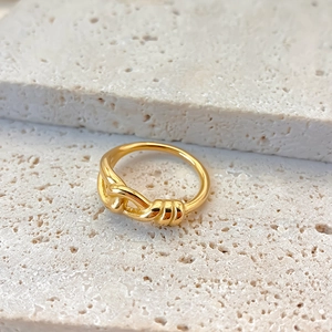 Primo piano di un anello a nodo minimalista in acciaio inossidabile dorato su pietra