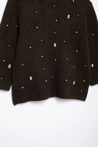Close-up detail of dark knit cardigan with golden studs and crystal rhinestone embellishments