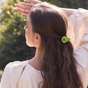 Detail of a green avocado hair claw clip worn on a half-up hairstyle in natural light