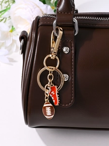 Detail of red boot and brown rugby ball keychain charm on a brown leather handbag