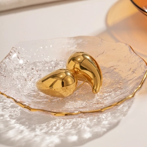 Detailed close-up of thick gold-plated hollow teardrop earrings on a glass tray