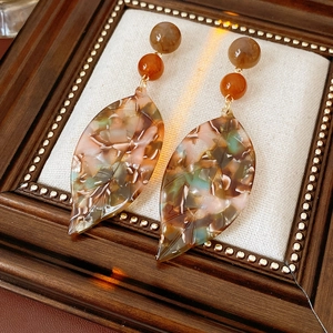 Close-up of vintage resin leaf earrings with amber beads on an elegant display base
