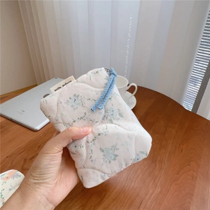 Close-up of floral quilted cotton pouch with blue woven zipper pull and soft padding