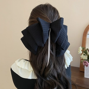 Close-up of black lace bow hair clip with sparkling rhinestone tassels worn by a model