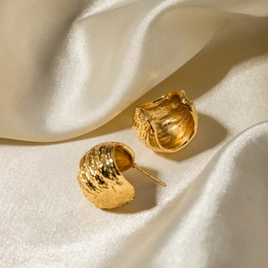 Detailed view of gold C-shaped earrings with hammered texture on beige silk background