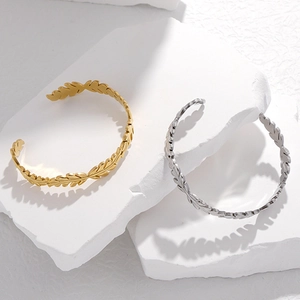 Bracciali rigidi aperti a forma di foglia in oro e argento su sfondo di pietra bianca