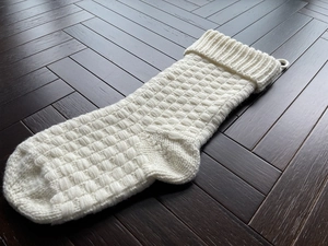 Detailed view of a white knitted Christmas stocking with square texture on wooden floor
