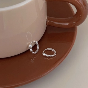 Detail of silver textured hoop earrings placed next to a beige ceramic mug on a wooden tray