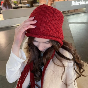 Close-up detail of red chunky knit beanie with handmade tassel and braided texture
