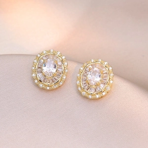 Macro shot of gold oval stud earrings with radiant zircons on champagne silk