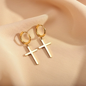 Close-up of polished gold-plated cross charms on silk fabric for a luxury earring detail