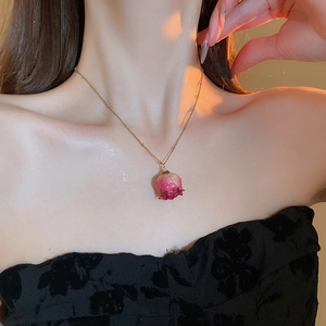 Detail of elegant gold necklace featuring a real dried pink rose bud pendant on model