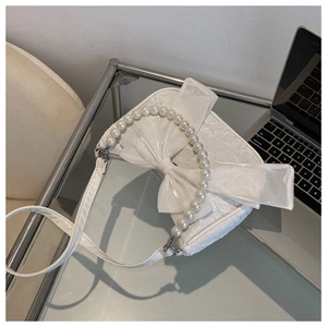 Detailed view of the white textured fabric bag with large bow and pearl handle