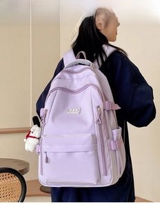 Detail view of large lavender backpack with side straps and plush pendant on model