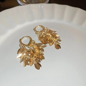 Close-up of golden leaf tassel earrings with multi-layered design on a white plate