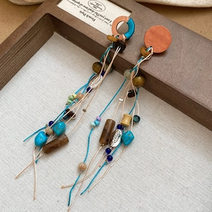 Detail of bohemian tassel earrings with wooden beads and turquoise accents on linen background