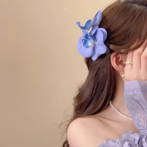 Detail of blue and violet orchid hair clip with central pearl worn by a model
