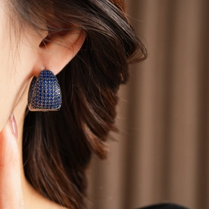 Detail of a C-shaped earring with pavé-set deep blue zircons on a silver base