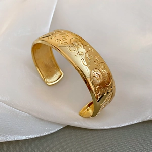 Close-up of golden oval cuff bracelet featuring intricate embossed scroll patterns