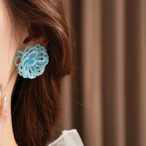 Close-up of blue beaded flower earrings with silver needles worn by a female model