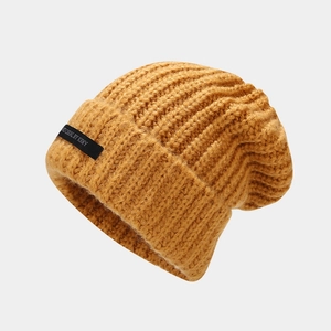 Detalle de gorro de punto grueso amarillo mostaza con etiqueta negra y textura acanalada