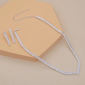 Detail view of silver cubic zirconia necklace and dangling earrings set on textured sand