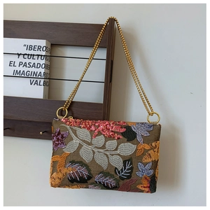 Detail showing floral embroidery and sequins on brown clutch bag with gold chain strap