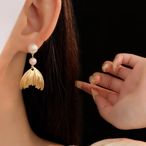 Close-up of golden fishtail earrings with elegant white pearls on a model ear