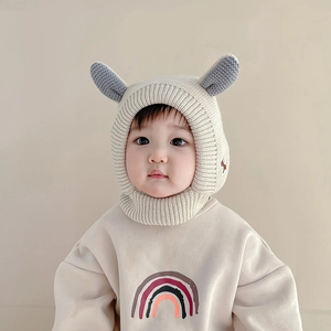 Détail d'un bonnet à oreilles tricoté pour bébé beige et d'un sweat-shirt assorti